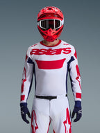Alpinestars 2026 Racer Riway Gear Set, piloto de motocross con jersey blanco con logotipos rojos y detalles en azul marino, pantalones blancos a juego con gráficos rojos, casco rojo con gafas blancas, guantes azul marino, conjunto profesional coordinado para carreras off-road.