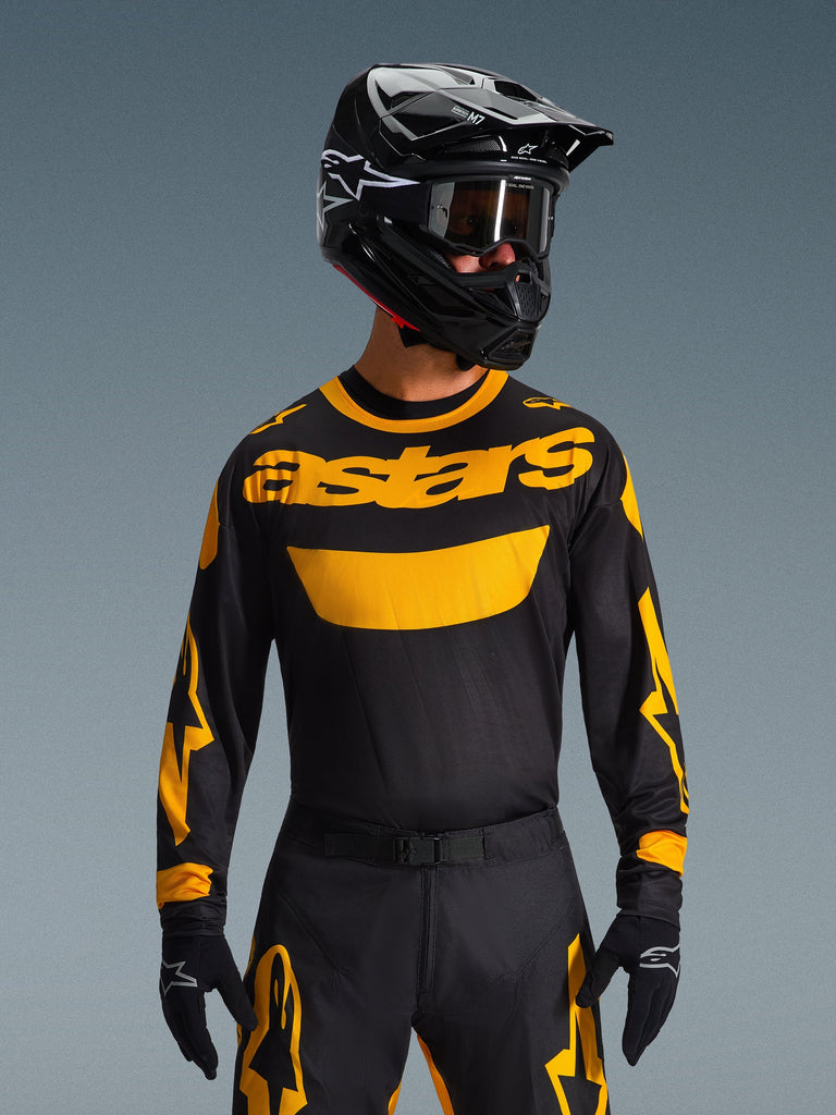 Motocross rider wearing the Alpinestars 2026 Racer Riway Jersey in Yellow and Black, featuring a bold yellow 'astars' logo across the chest, paired with coordinating black and yellow pants, a black helmet with goggles, and black gloves, professional off-road racing gear set.