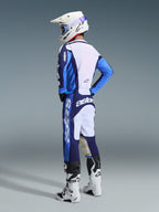 Motocross rider from a rear-side view wearing the Alpinestars 2026 Racer Riway Gear Set in UCLA Blue and White, featuring a blue and white jersey with 'astars' branding, matching blue and white pants, a white motocross helmet with blue goggles, and white and black Tech series boots.