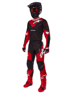 Piloto de motocross con equipamiento completo de competición que incluye el jersey Alpinestars 2025 Racer Veil en negro y rojo brillante, pantalones a juego, botas rojas, casco negro con gafas rojas y guantes rojos y negros, look coordinado de alto rendimiento para carreras off-road