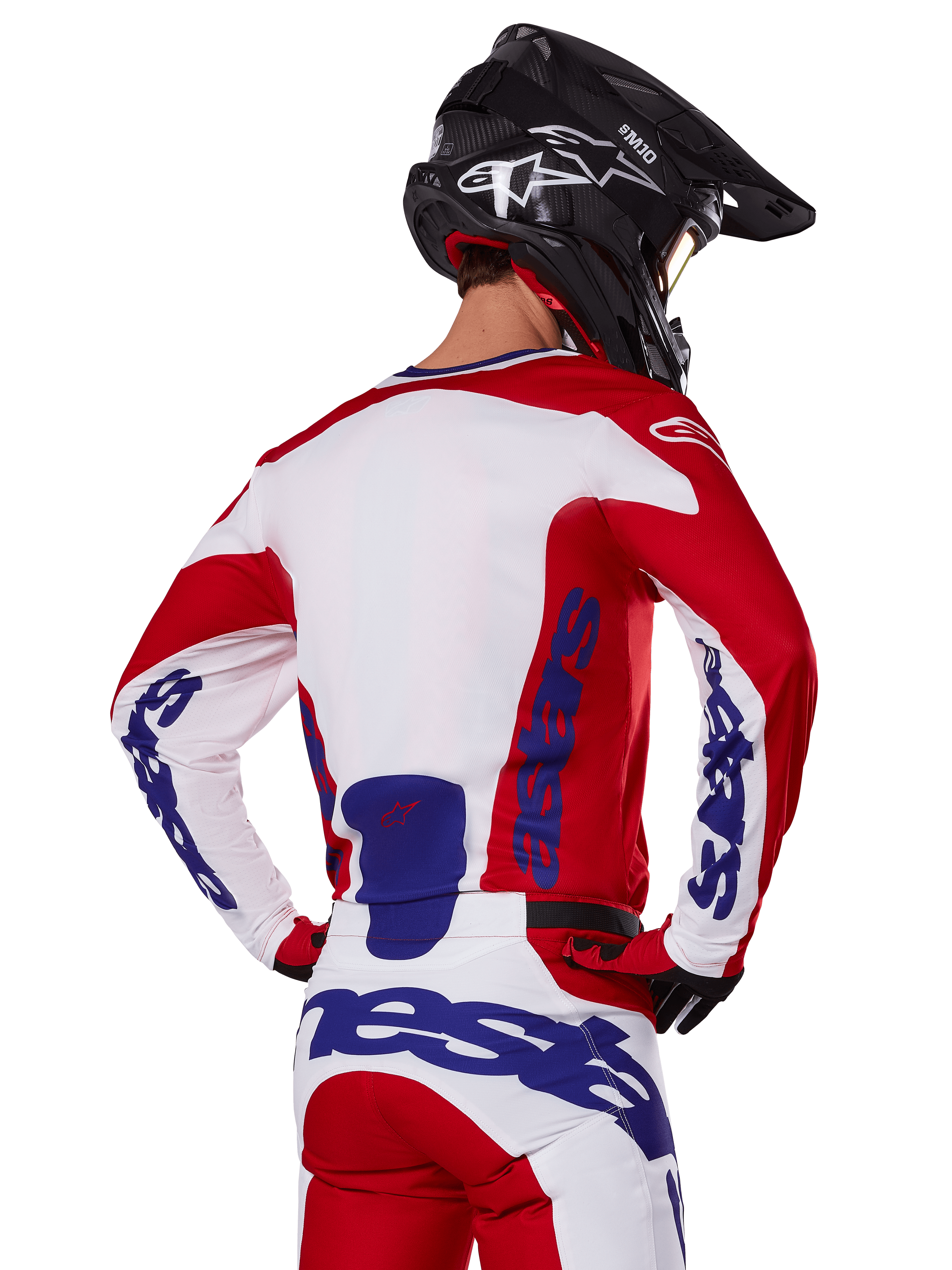 Alpinestars 2025 Racer Veil Jersey y pantalones, conjunto de equipamiento de motocross, rojo brillante, blanco y azul, vista trasera de un piloto con el equipo a juego y casco de motocross negro, con logotipos llamativos de Alpinestars en azul, ropa técnica para carreras off-road