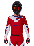 Alpinestars 2025 Racer Veil Jersey, jersey de motocross de manga larga, rojo, blanco y azul, usado con casco negro y gafas naranjas, guantes y pantalones rojos a juego, diseño de alto rendimiento para conducción off-road
