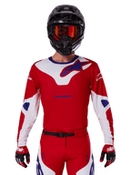 Alpinestars 2025 Racer Veil Jersey, jersey de motocross de manga larga, rojo, blanco y azul, usado con casco negro y gafas naranjas, guantes y pantalones rojos a juego, diseño de alto rendimiento para conducción off-road