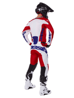 Piloto de motocross visto desde atrás vistiendo el jersey y los pantalones Alpinestars Racer Veil 2025 en rojo y blanco, con logotipos en azul, casco negro y botas blancas, conjunto completo de equipamiento para carreras off-road