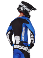 Alpinestars 2025 Racer Veil Gear Set, equipo de motocross, azul, negro y blanco, vista trasera de un piloto con jersey y pantalones con logotipos destacados, casco blanco y negro, conjunto coordinado para carreras todoterreno