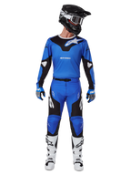 Piloto de motocross con el conjunto de equipo Alpinestars 2025 Racer Veil, jersey azul y negro con pantalones a juego, casco negro con gafas blancas, botas blancas y negras, atuendo de carreras coordinado para motocross off-road.