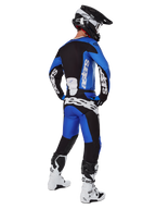 Piloto de motocross con equipamiento de carreras completo visto desde atrás, jersey Racer Veil 2025 y pantalones a juego en azul y negro, con logotipo de Alpinestars en blanco, casco negro, botas blancas y negras, conjunto coordinado para carreras off-road