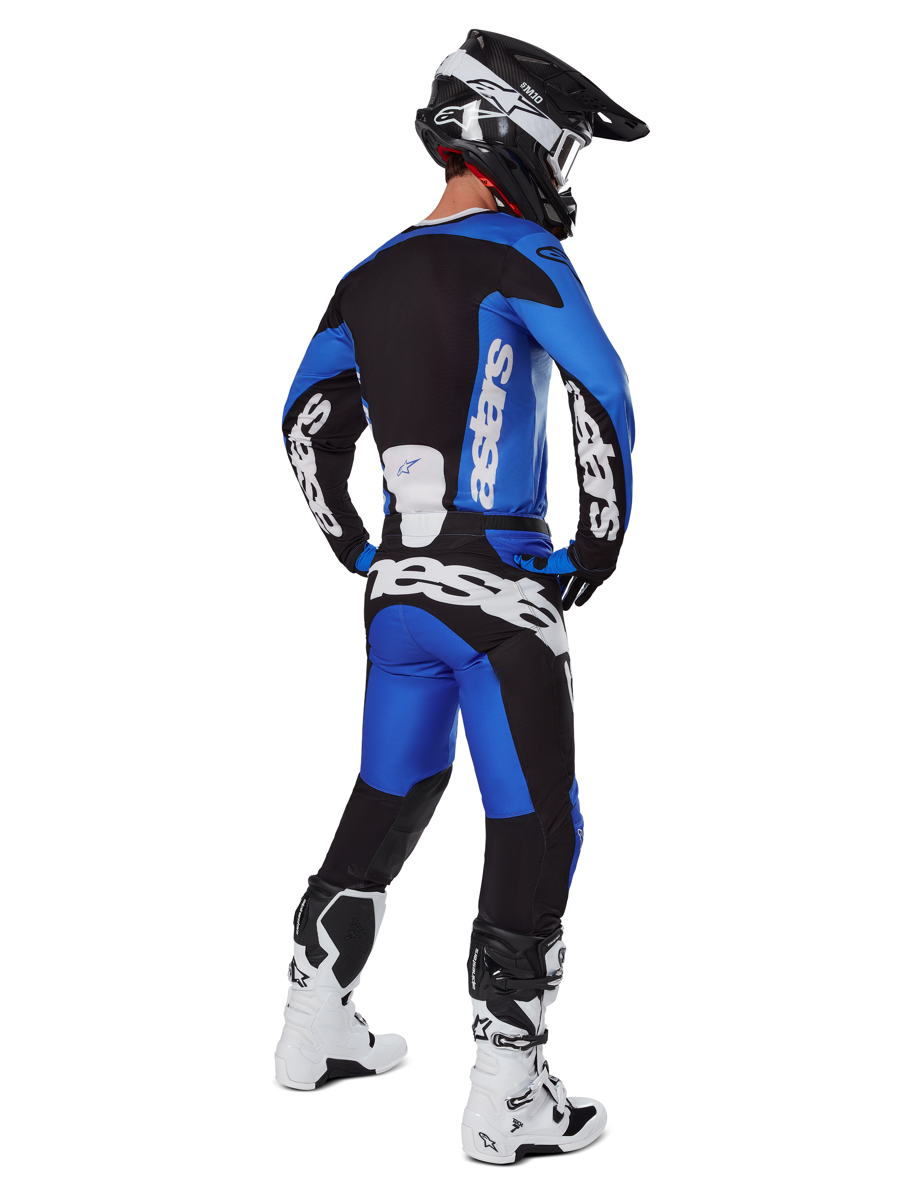 Piloto de motocross con equipamiento de carreras completo visto desde atrás, jersey Racer Veil 2025 y pantalones a juego en azul y negro, con logotipo de Alpinestars en blanco, casco negro, botas blancas y negras, conjunto coordinado para carreras off-road