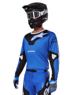 Alpinestars 2025 Racer Veil Gear Set, conjunto de equipo de motocross, jersey azul con gráficos en negro y blanco, usado con pantalones a juego, casco negro, gafas blancas y guantes azules, indumentaria técnica para carreras todoterreno