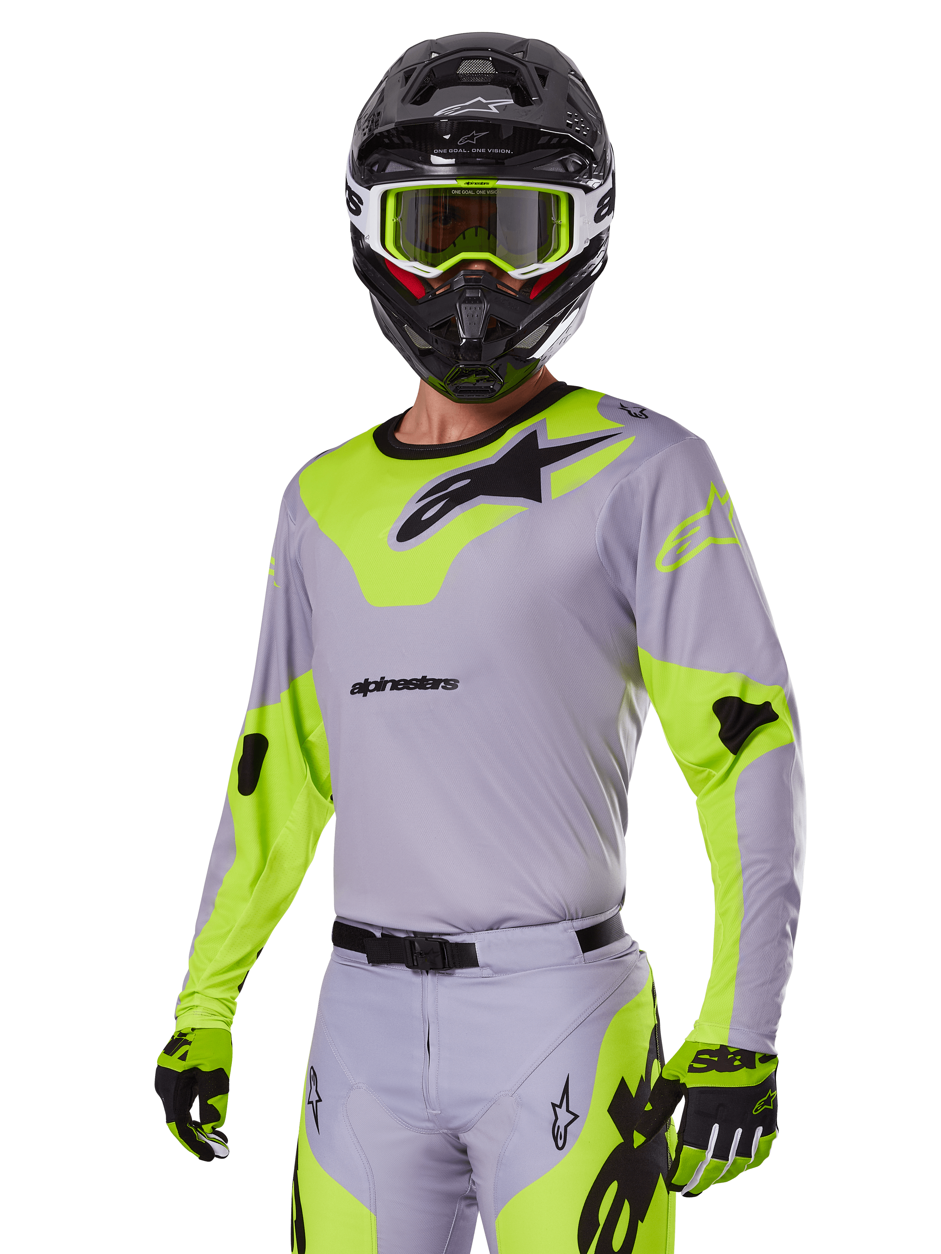 Piloto de motocross con el conjunto Alpinestars 2025 Racer Veil en gris y verde flúor, jersey y pantalones gris claro con paneles llamativos en verde neón y logotipos de Alpinestars en negro, coordinado con guantes a juego y un casco negro con gafas verde neón, equipamiento profesional para carreras todoterreno.