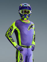 Piloto de motocross vistiendo el Jersey Racer Portl 2026 de Alpinestars, en morado y amarillo flúor, casco a juego en morado y amarillo con gafas blancas, guantes en morado y amarillo, conjunto completo de equipamiento coordinado para carreras off-road