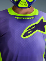 Alpinestars 2026 Racer Portl Jersey, jersey de motocross, morado y amarillo flúor, primer plano de la zona del pecho con un gran logotipo de Alpinestars perfilado en amarillo, cuello elástico con marca, tejido técnico de polifibra que absorbe la humedad