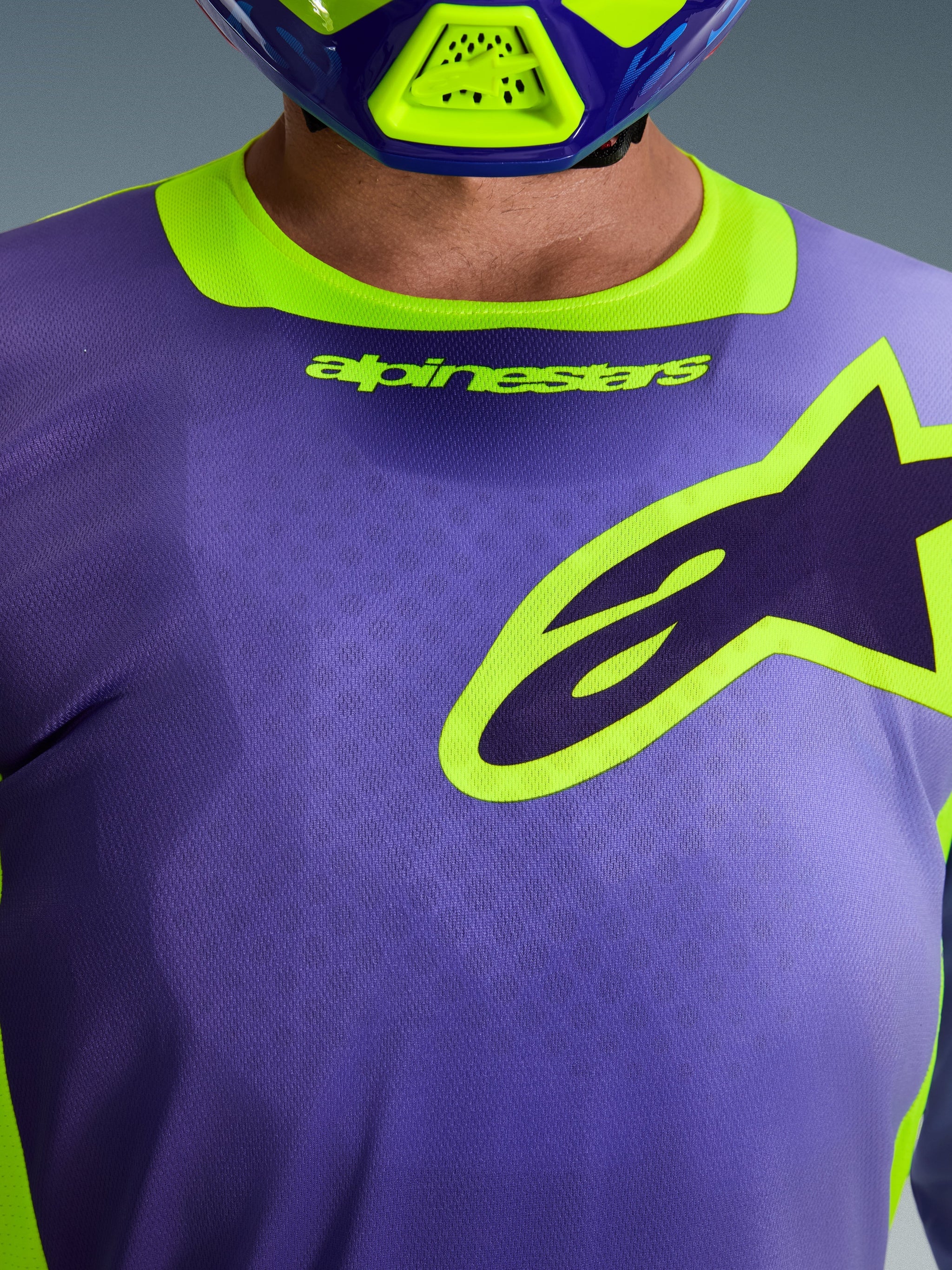 Alpinestars 2026 Racer Portl Jersey, jersey de motocross, morado y amarillo flúor, primer plano de la zona del pecho con un gran logotipo de Alpinestars perfilado en amarillo, cuello elástico con marca, tejido técnico de polifibra que absorbe la humedad