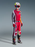 Motocross rider wearing the Alpinestars 2026 Racer Portl Gear Set, featuring a Red and White jersey with bold 'Astars' branding on the sleeve, matching Red and White pants, a coordinated white and yellow helmet with red-framed goggles, and gray and black motocross boots, complete outfit for off-road racing.