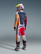 Motocross rider wearing complete racing gear from behind, Alpinestars 2026 Racer Portl Jersey in Red Light Gray and Dark Green with orange and maroon panels, matching white and red pants, gray and black boots with pink details, multicolored helmet, coordinated off-road racing outfit.