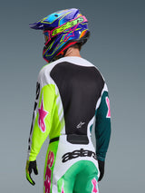 Piloto de motocross visto desde atrás vistiendo el Jersey Alpinestars 2026 Racer Portl en verde, blanco y negro, con logotipos de estrellas en rosa, combinado con pantalones a juego y un colorido casco azul y púrpura, equipamiento de carreras coordinado para rendimiento off-road.