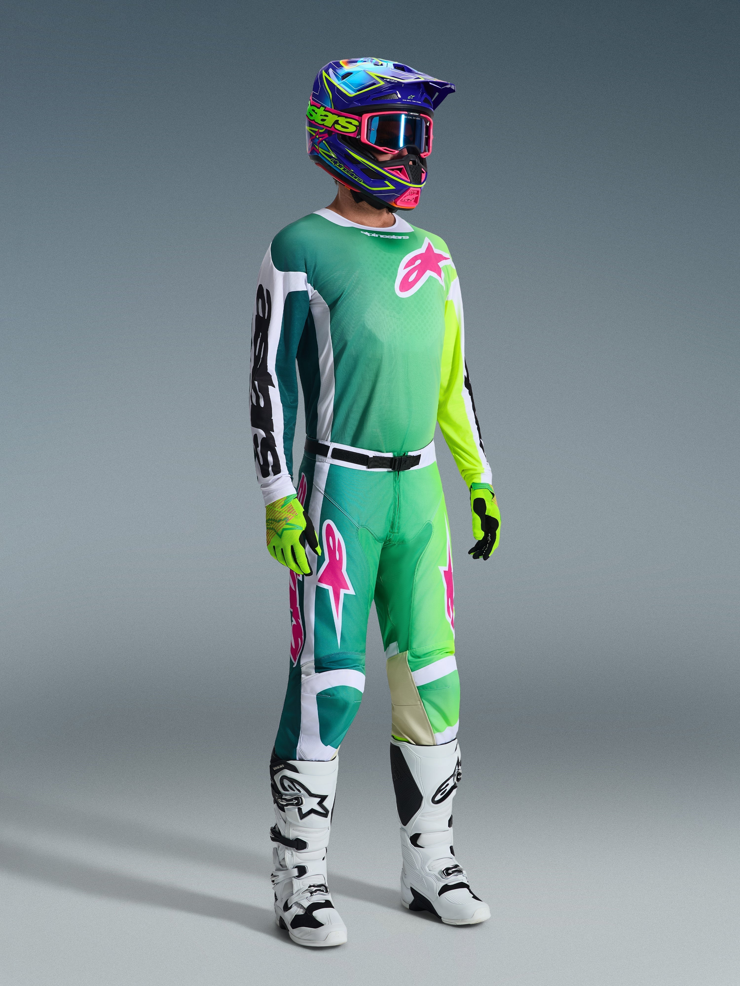 Piloto de motocross con equipamiento de carreras completo, Jersey Racer Portl 2026 en verde con mangas blancas y negras y logotipo rosa, pantalones verdes a juego con detalles en rosa, casco multicolor con gafas, botas blancas y negras y guantes verdes, conjunto coordinado para carreras todoterreno