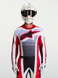 Alpinestars Techstar Maven, jersey de motocross para hombre, rojo fuego y blanco, ajuste atlético y tejido ligero, mostrado en un modelo con equipo de carreras MX