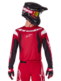 Alpinestars Jersey Fluid Haul 2025, jersey de motocross, rojo brillante y negro, usado como parte de un conjunto completo con pantalones y guantes a juego, casco negro con gafas de lente amarilla, logotipos y marcas en blanco, ropa de carreras off-road de alto rendimiento