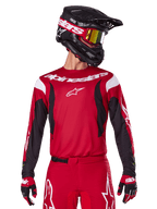 Alpinestars Jersey Fluid Haul 2025, jersey de motocross, rojo brillante y negro, usado como parte de un conjunto completo con pantalones y guantes a juego, casco negro con gafas de lente amarilla, logotipos y marcas en blanco, ropa de carreras off-road de alto rendimiento