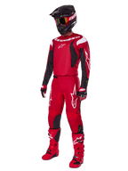 Piloto de motocross con el conjunto de equipamiento Alpinestars Fluid Haul 2025, rojo brillante con detalles en negro y blanco, equipo completo que incluye jersey, pantalones, casco, botas y guantes, diseñado para el rendimiento y la protección todoterreno