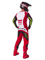 Piloto de motocross visto desde atrás vistiendo el conjunto Alpinestars 2025 Fluid Haul, rojo brillante y negro con paneles blancos, logotipos en amarillo neón en mangas y pantalones, botas rojas y casco negro a juego, equipamiento profesional completo para carreras todoterreno.