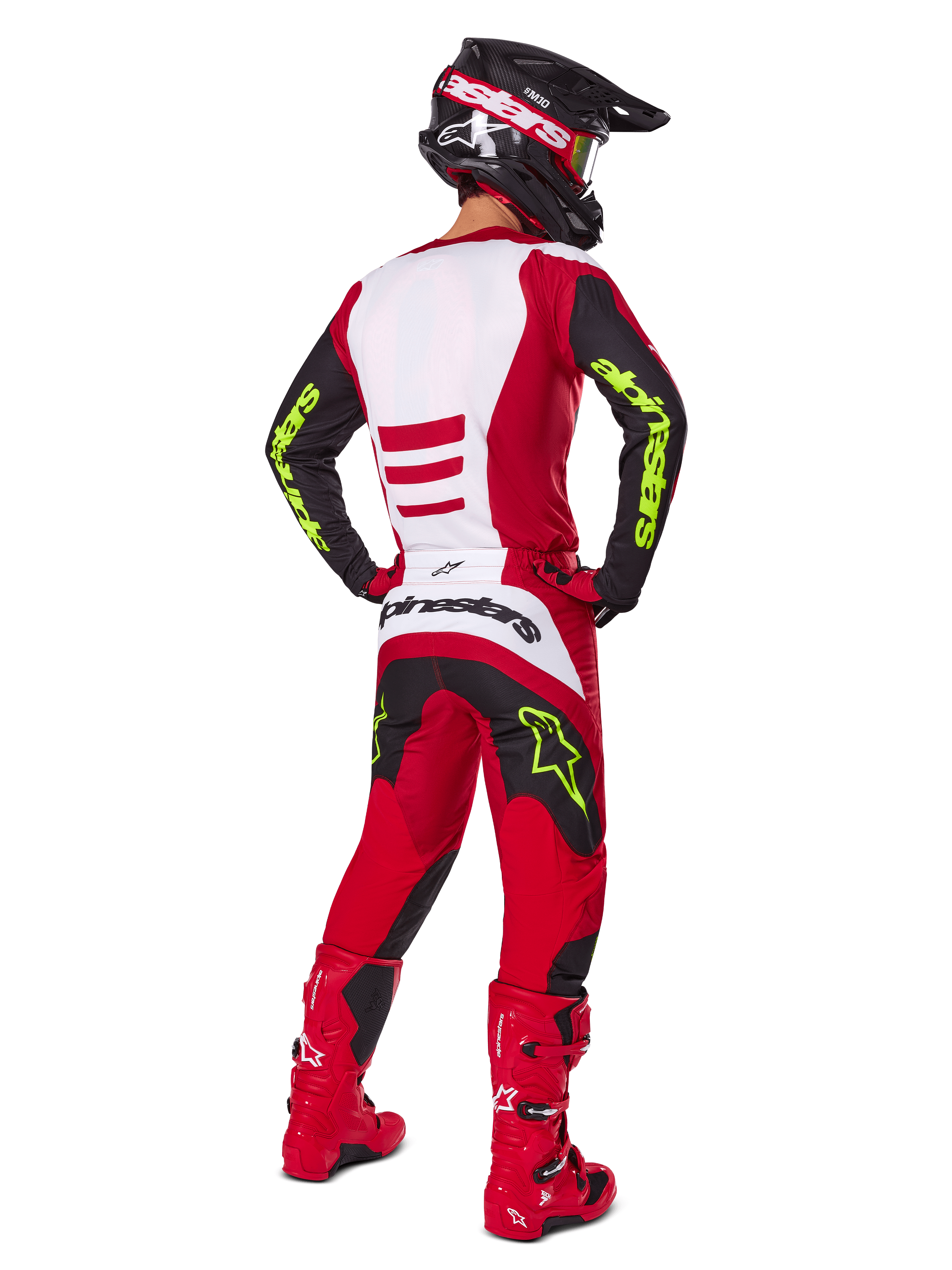 Piloto de motocross visto desde atrás vistiendo el conjunto Alpinestars 2025 Fluid Haul, rojo brillante y negro con paneles blancos, logotipos en amarillo neón en mangas y pantalones, botas rojas y casco negro a juego, equipamiento profesional completo para carreras todoterreno.