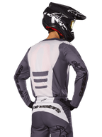 Piloto de motocross visto desde atrás con el conjunto Alpinestars 2025 Fluid Haul, jersey y pantalones en gris y blanco, casco negro con gráficos blancos, gafas amarillas, atuendo de motocross coordinado