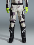 Alpinestars 2026 Racer Lahnd Pants, pantalones de motocross, patrón Sand Camo con gráficos abstractos en gris y morado, usados con guantes amarillo neón y botas negras, con logotipos de estrellas negras en los muslos y un cinturón negro, equipamiento duradero para carreras off-road