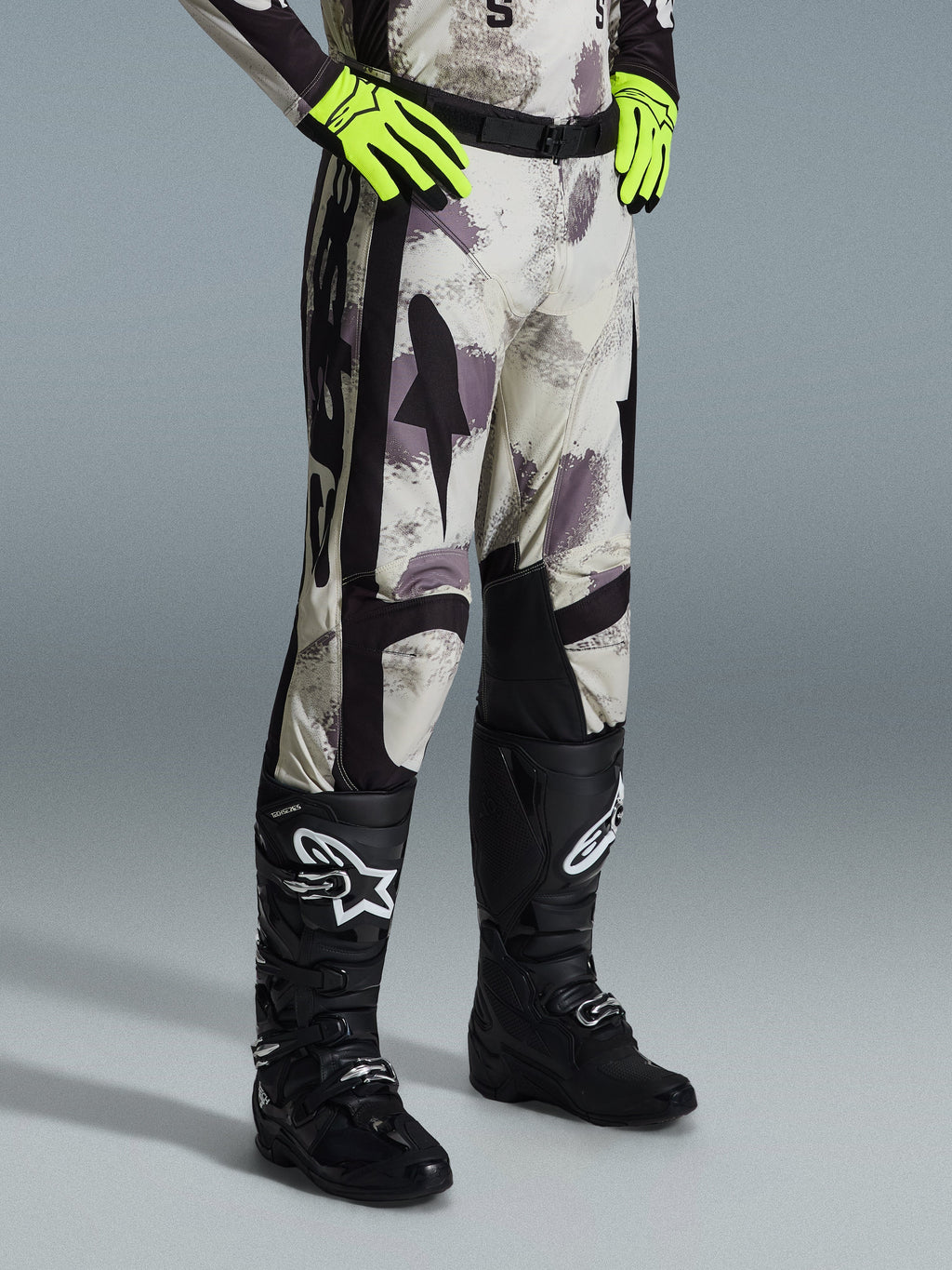 Alpinestars 2026 Racer Lahnd Pants, pantalones de motocross, Sand Camo, usados con guantes amarillo neón y botas de motocross negras, con un patrón de camuflaje abstracto y paneles laterales negros, diseño ergonómico off-road