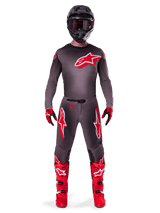 Motocross rider wearing complete racing gear, 2025 Supertech Lipan Jersey in Smoke Bright Red, matching grey pants with red logos, bright red boots, black helmet with goggles, and red and black gloves, professional motocross outfit.