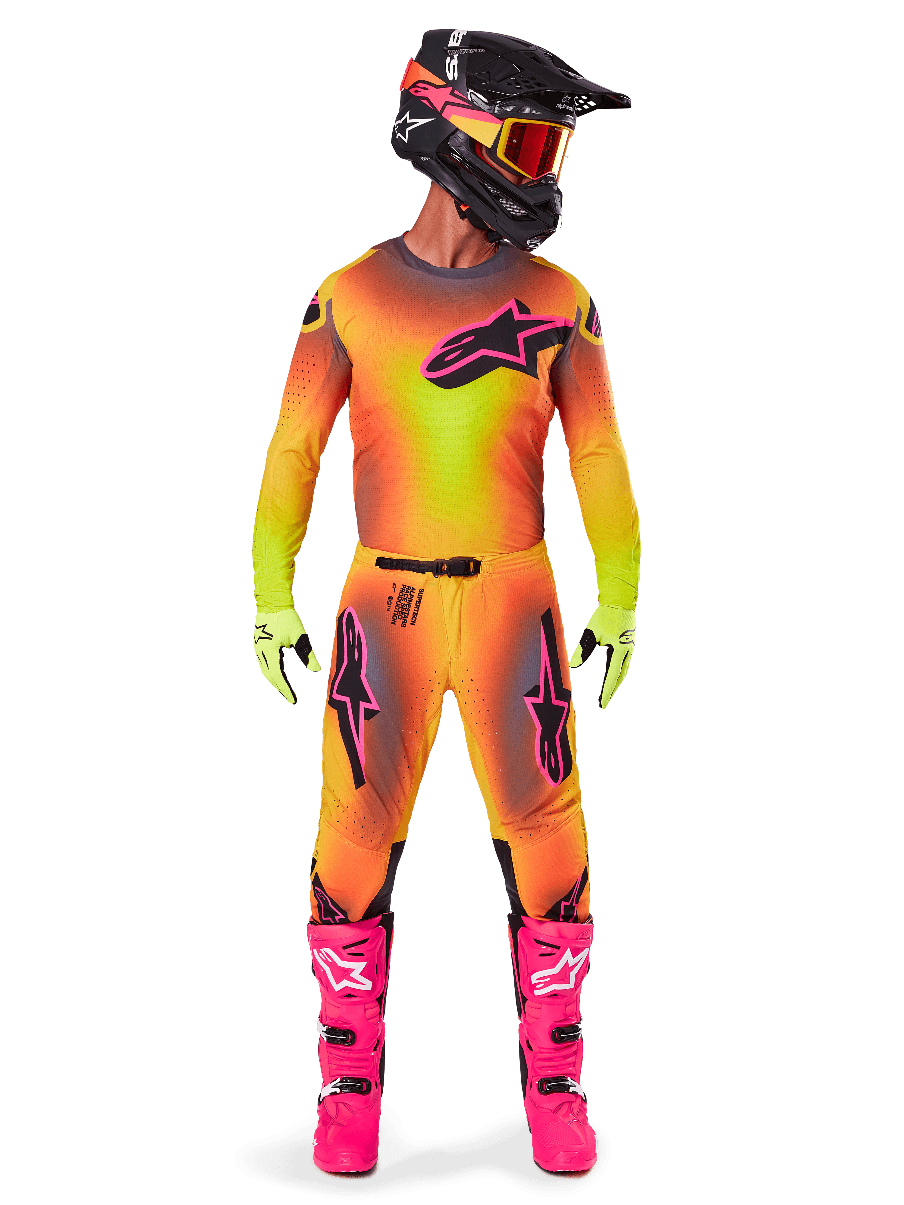 Piloto de motocross con equipamiento completo de competición, Jersey y Pantalones Supertech Lipan 2025 en un degradado amarillo y naranja con detalles en rosa, casco negro con gráficos rosas a juego, botas rosa brillante y guantes verde lima, conjunto coordinado de Alpinestars para carreras off-road.