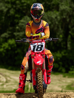 Piloto de motocross sentado en una moto Honda roja con el número 18, vistiendo el jersey Alpinestars Supertech Lipan 2025 y pantalones a juego en amarillo y rosa, botas Alpinestars rosa brillante, casco Red Bull, equipo de competición profesional para rendimiento todoterreno.