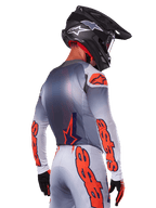 Motocross rider from the back wearing Alpinestars 2025 Supertech Lipan Jersey and Gear Set, Gray with Orange Fluo accents, featuring bold branding on back and sleeves, black helmet, and black gloves, coordinated motocross racing outfit
