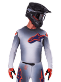Alpinestars Supertech Lipan Jersey 2025, jersey de motocross de manga larga, gris con detalles en naranja y azul marino, camiseta técnica con perforaciones de ventilación, usado con casco negro y guantes rojos, diseño de competición estilizado