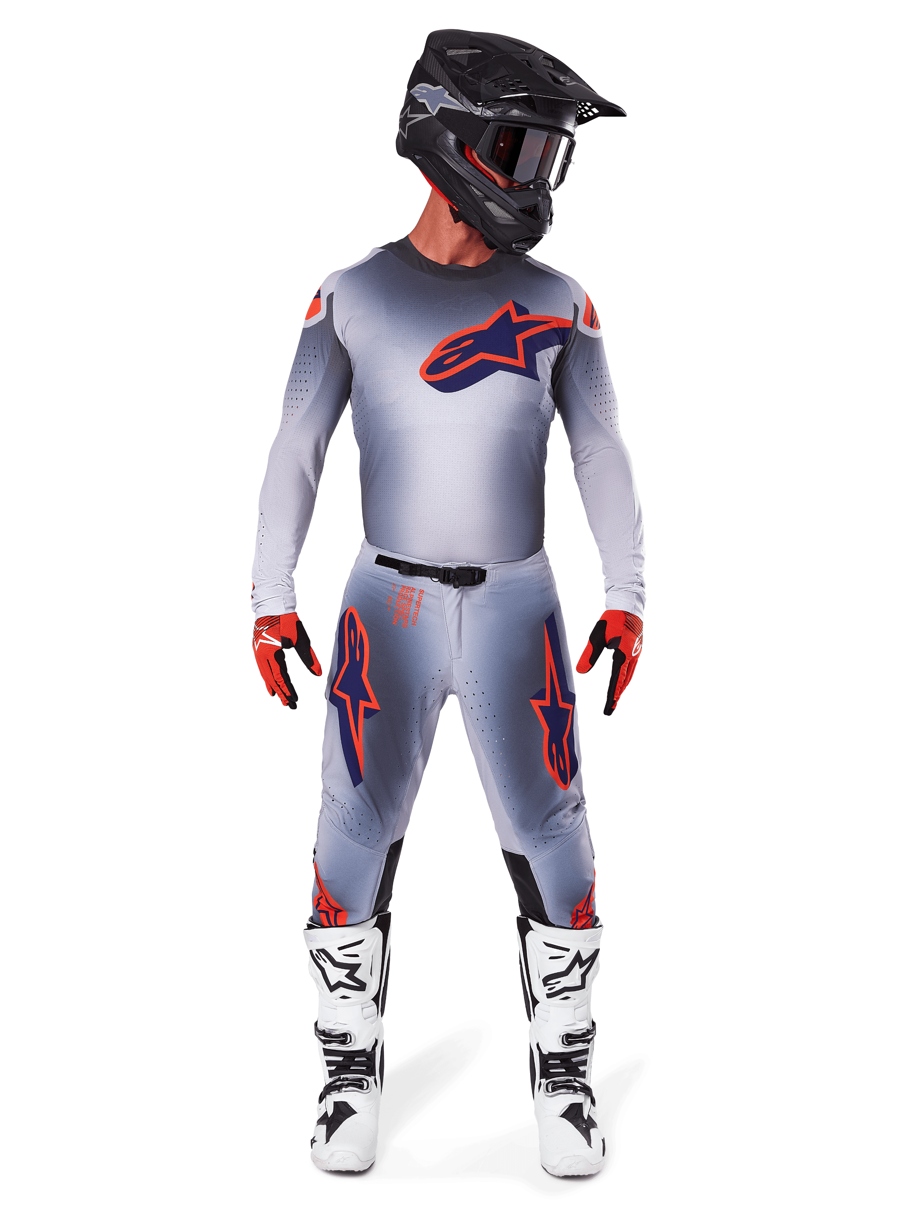 Motocross rider wearing the 2025 Supertech Lipan Gear Set in Gray Orange Fluo, featuring a gray jersey with orange accents and a navy Alpinestars logo, matching gray pants with large thigh logos, a matte black helmet, white and black boots, and red and black gloves, complete pro-level racing outfit.
