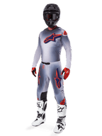 Piloto de motocross vistiendo el Jersey Alpinestars Supertech Lipan 2025 en gris y naranja flúor, pantalones grises a juego con detalles en naranja, casco negro, botas blancas y negras, y guantes naranjas y negros, conjunto de equipamiento profesional para carreras off-road