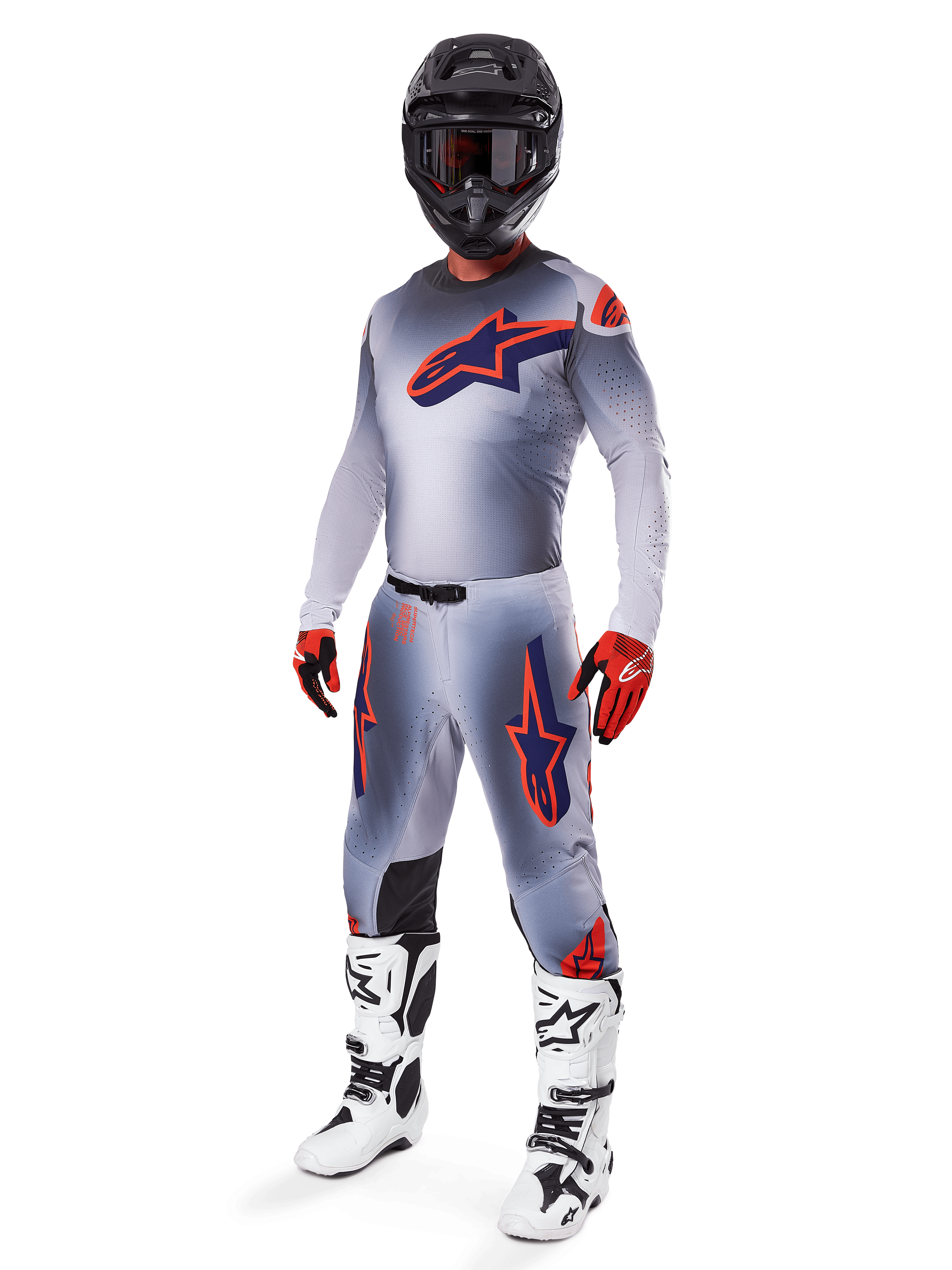 Piloto de motocross vistiendo el Jersey Alpinestars Supertech Lipan 2025 en gris y naranja flúor, pantalones grises a juego con detalles en naranja, casco negro, botas blancas y negras, y guantes naranjas y negros, conjunto de equipamiento profesional para carreras off-road