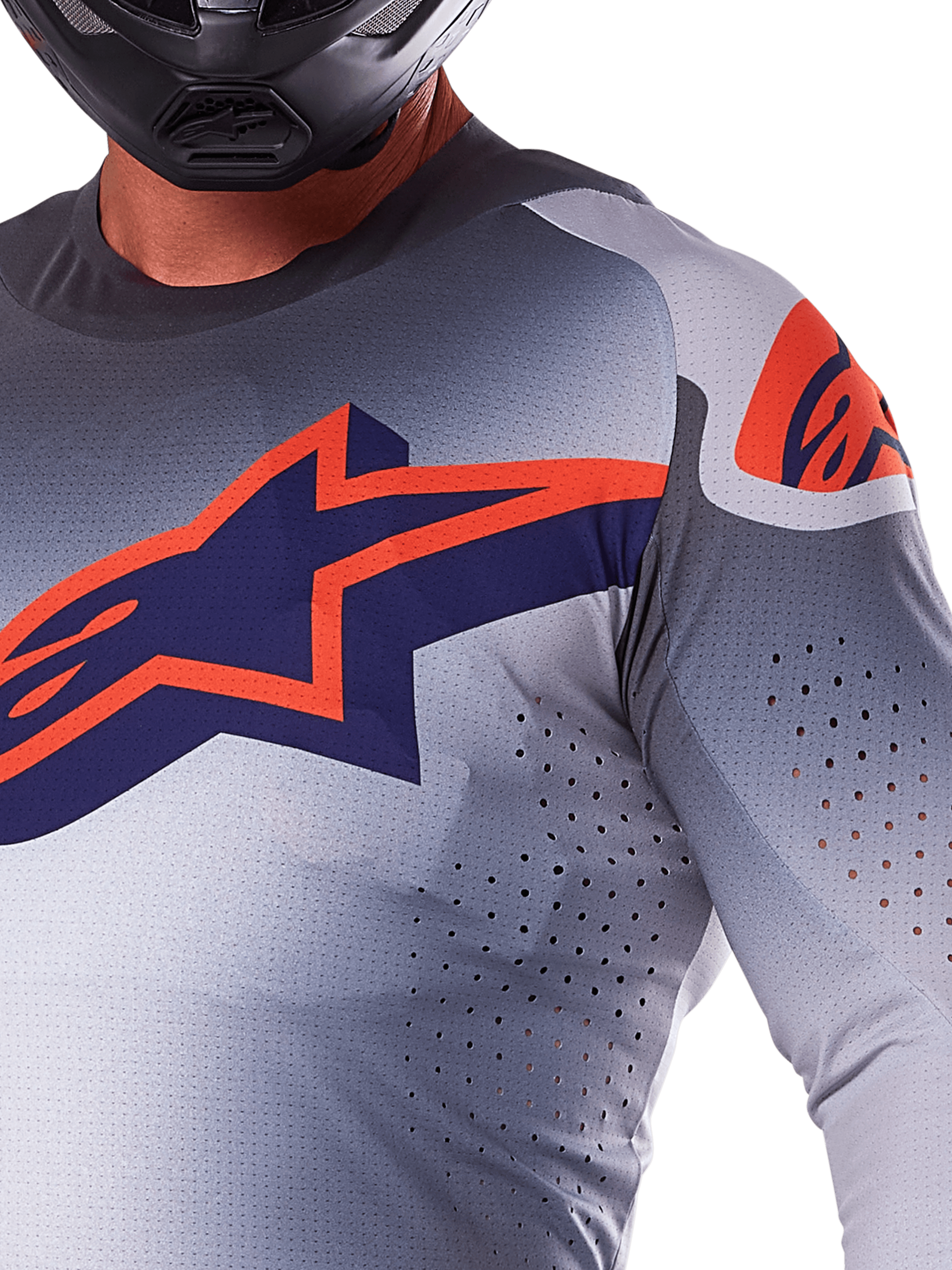 Primer plano de un piloto con el Jersey Alpinestars 2025 Supertech Lipan, jersey de motocross, gris y naranja flúor, con un gran logotipo naranja de Alpinestars en el pecho, perforaciones láser para ventilación y un casco negro, equipamiento de competición profesional.