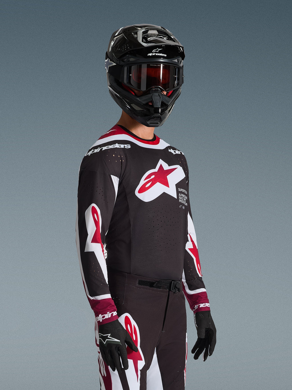 Piloto de motocross con el jersey Alpinestars Supertech AFD Vista 2026 en negro, rojo y blanco, con un gran logotipo de estrella roja en el pecho y perforaciones cortadas con láser, combinado con un casco negro y pantalones de carreras a juego para un rendimiento todoterreno