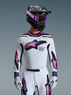 Piloto de motocross con el Jersey Supertech AFD Vista 2026 en blanco, púrpura y negro, con un casco negro con detalles de marca en rosa, gafas púrpuras y guantes blancos a juego, equipamiento de ajuste atlético diseñado para el rendimiento profesional en carreras off-road