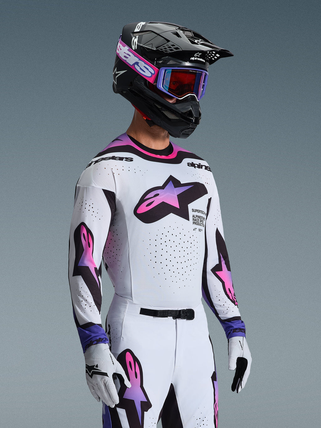 Piloto de motocross con el Jersey Supertech AFD Vista 2026 en blanco, púrpura y negro, pantalones a juego en blanco y púrpura, casco negro con gafas púrpuras y guantes blancos, equipamiento completo profesional para carreras off-road.