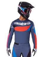 Alpinestars 2025 Techstar Dreem Jersey, jersey de motocross, gris con detalles en azul, rojo y rosa, con perforaciones cortadas por láser y un logotipo grande en el pecho, usado con pantalones a juego y casco de carreras negro