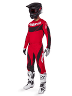 Full-body view of a motocross rider in the 2025 Techstar Dreem Gear Set in Bright Red and Black, featuring a performance jersey with white branding, matching stretch ripstop pants, a black helmet with a red visor, white and black gloves, and white Tech boots, specialized racing outfit for off-road competition.