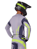 Motocross rider from the rear wearing Alpinestars 2025 Techstar Dreem Gear Set, Gray jersey and pants with vibrant neon yellow-green branding, matching black helmet with neon graphics, professional motocross racing outfit