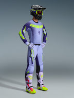 Alpinestars 2026 Supertech Scenz Gear Set, Motocross rider wearing full racing apparel, Light purple jersey with dark purple sleeves and neon yellow accents, matching lavender pants, black helmet with neon yellow goggles, and lavender boots with neon green and red details, coordinated professional off-road outfit.