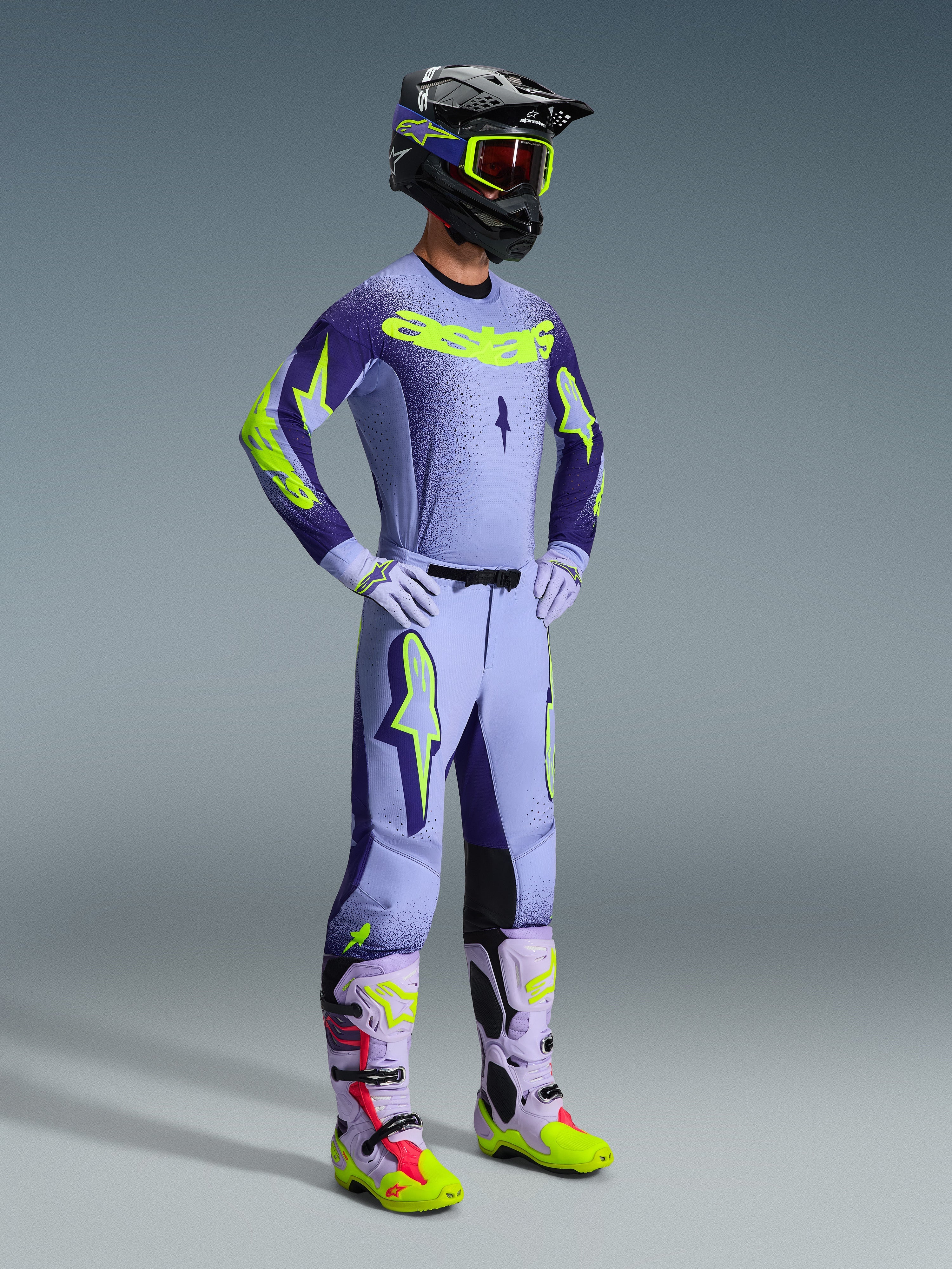 Alpinestars 2026 Supertech Scenz Gear Set, Motocross rider wearing full racing apparel, Light purple jersey with dark purple sleeves and neon yellow accents, matching lavender pants, black helmet with neon yellow goggles, and lavender boots with neon green and red details, coordinated professional off-road outfit.