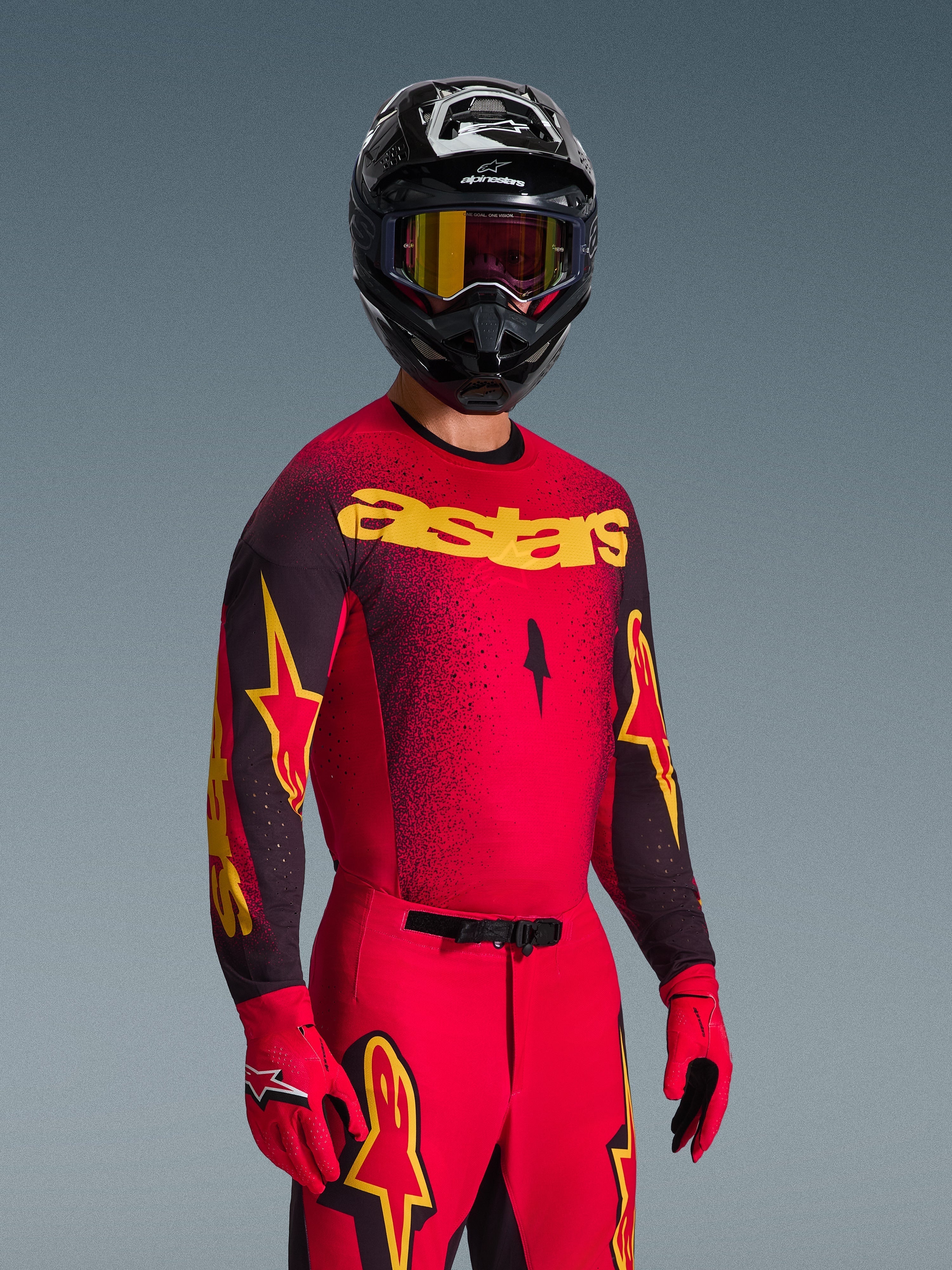 Piloto de motocross con el Jersey Alpinestars Supertech Scenz 2026 en rojo y negro con logotipo 'astars' amarillo, pantalones y guantes rojos a juego, casco negro con gafas, conjunto de equipamiento profesional para motocross off-road