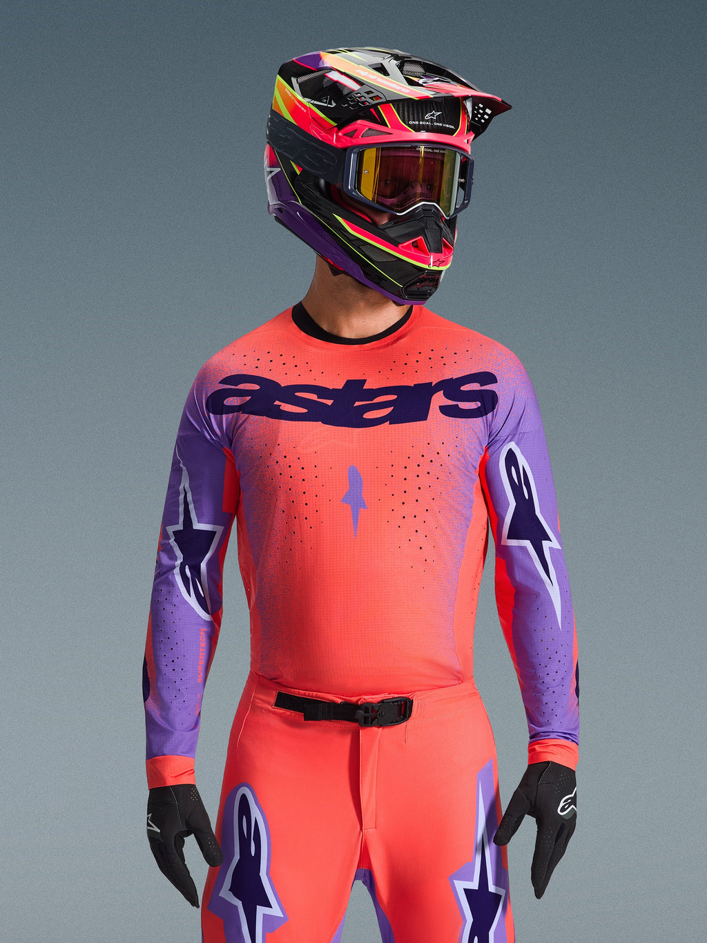 Alpinestars 2026 Supertech Scenz Jersey, camiseta de motocross, coral intenso y morado, con un gran logotipo 'astars' y diseños de estrellas en las mangas, usada con pantalones a juego y un casco multicolor, equipamiento todoterreno de alto rendimiento.