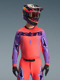 Alpinestars 2026 Supertech Scenz Jersey, camiseta de motocross, coral intenso y morado, con un gran logotipo 'astars' y diseños de estrellas en las mangas, usada con pantalones a juego y un casco multicolor, equipamiento todoterreno de alto rendimiento.